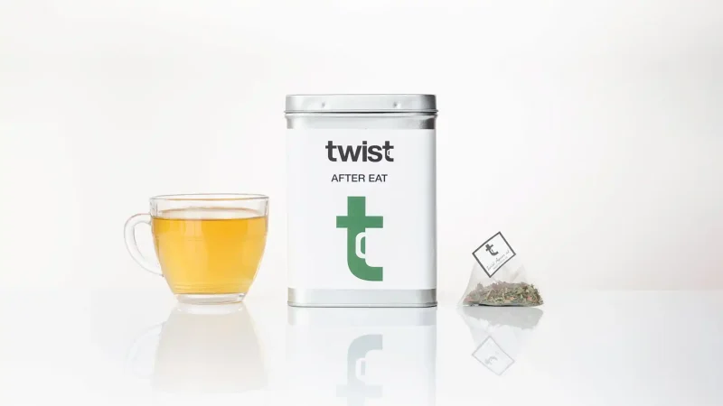 After Eat Tisane Regular Caddy next to a brewed cup of After Eat Tisane and an After Eat Tisane pyramid teabag