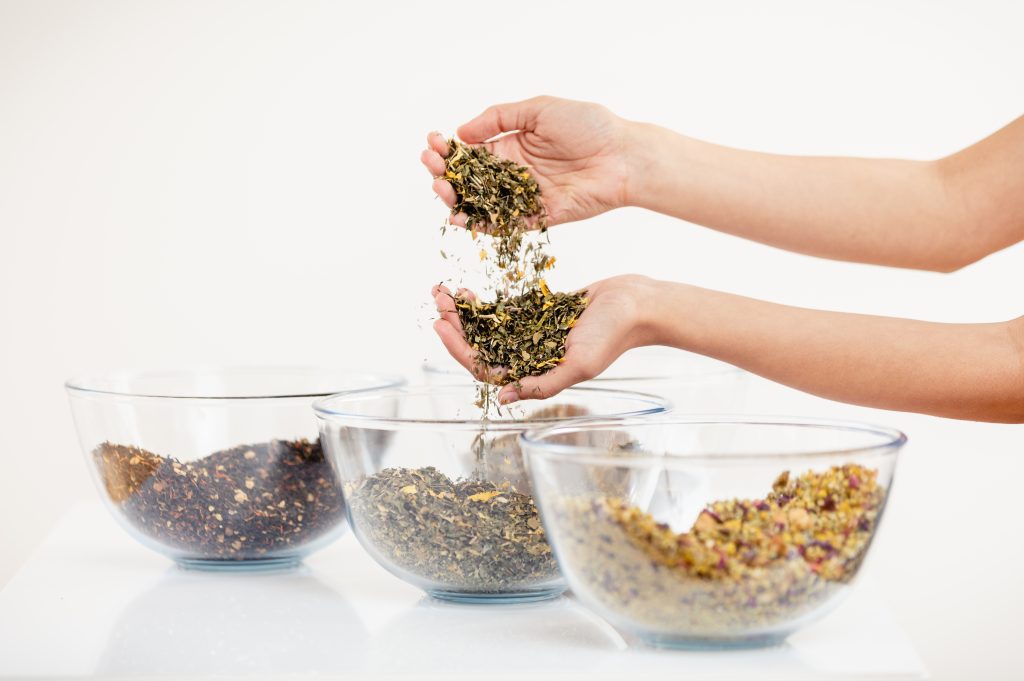 Hands pouring hand-blended loose leaf tea into glass bowls