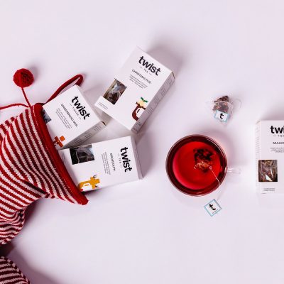 Twist Christmas tea cartons tumbling from a striped Christmas stocking beside a cup of tea