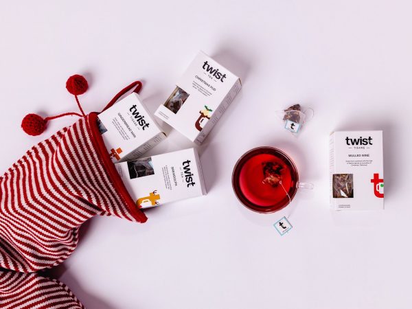 Twist Christmas tea cartons tumbling from a striped Christmas stocking beside a cup of tea