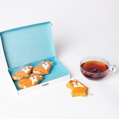 Twist gift box of four hand-iced King Corgi gingerbread biscuits beside a cup of tea
