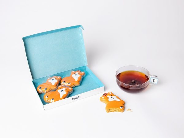 Twist gift box of four hand-iced King Corgi gingerbread biscuits beside a cup of tea