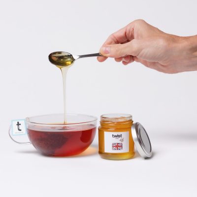 A spoon of Pollards Farm honey drizzling into a cup of Twist tea, with the honey jar