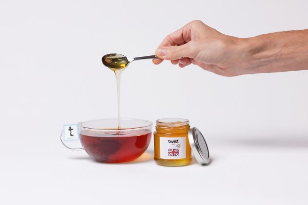 A spoon of Pollards Farm honey drizzling into a cup of Twist tea, with the honey jar
