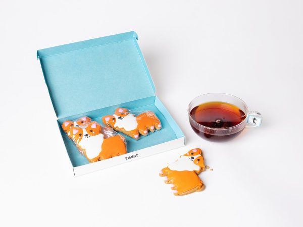 Twist gift box of four hand-iced Princess Corgi gingerbread biscuits beside a cup of tea