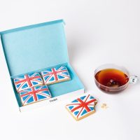 Twist gift box of four hand-iced Union Jack gingerbread biscuits beside a cup of tea