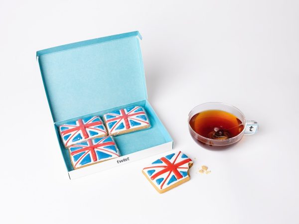 Twist gift box of four hand-iced Union Jack gingerbread biscuits beside a cup of tea