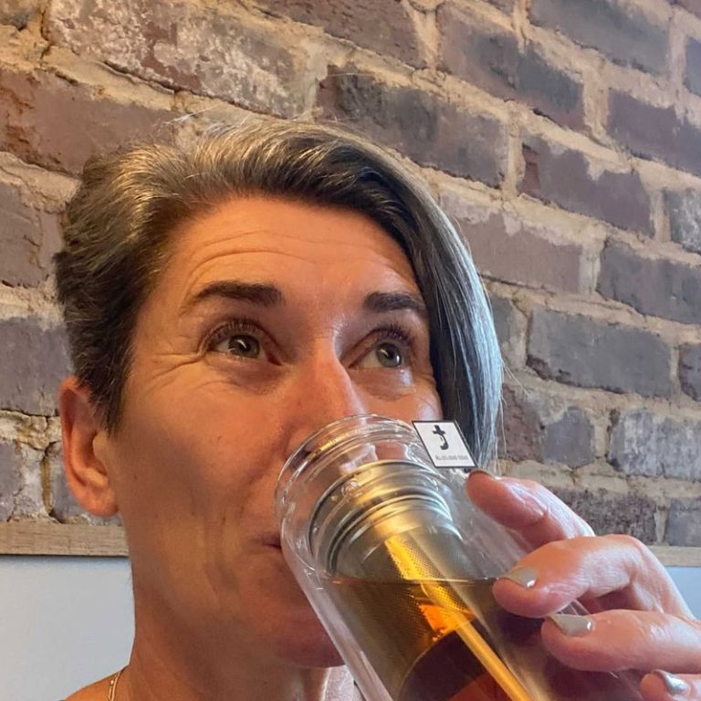 A woman drinking Twist tea from a glass infuser bottle